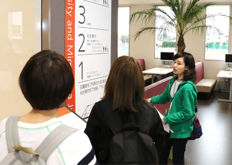 写真：階の案内板のそばに立つ3人の女子学生