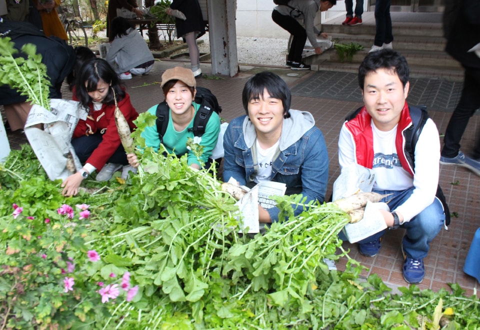 写真：無料野菜スタンドで並べられた野菜とそれを手に持つ学生たち
