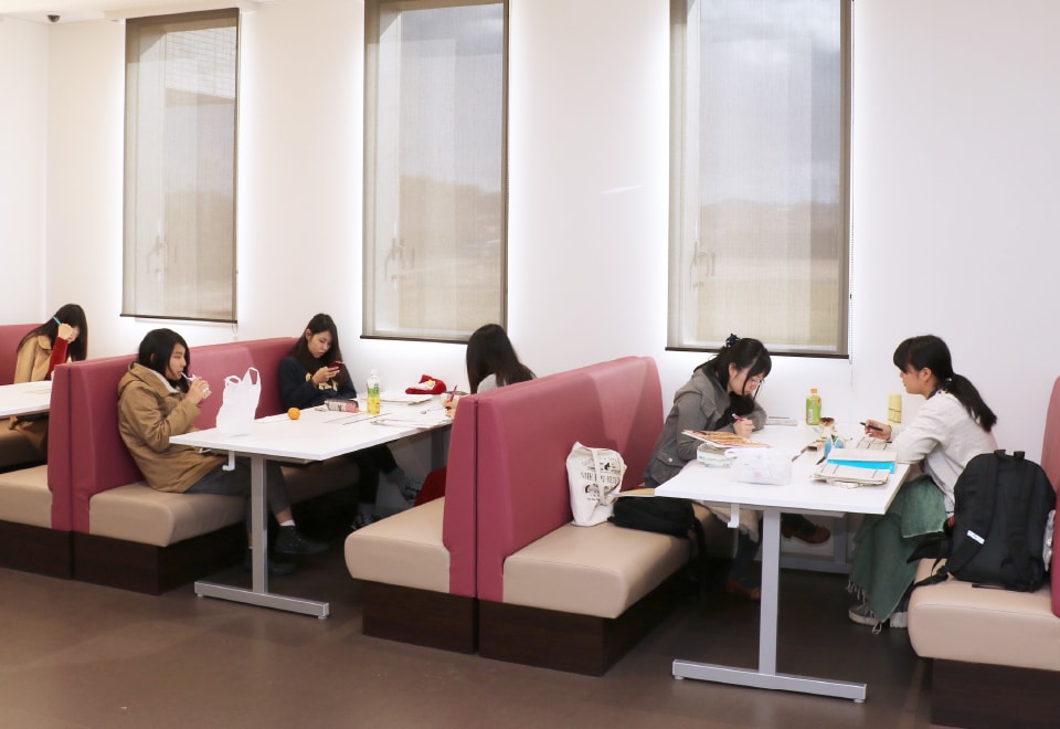 写真：オープンコモンズのダイナーテーブルでグループごとに向かい合わせに座る学生たち。勉強や休憩など思い思いに過ごしている。
