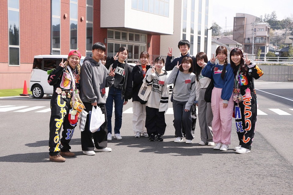 写真：学校の前でピースサインをして笑顔で並ぶ学生グループ
