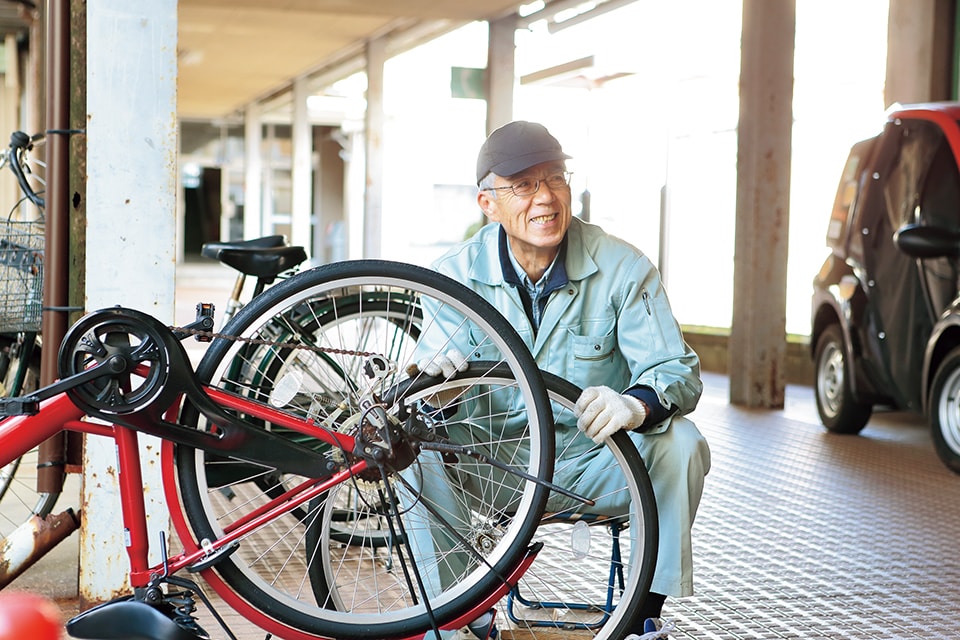 屋根のある場所で自転車を整備しながら笑顔を見せるシニアの男性