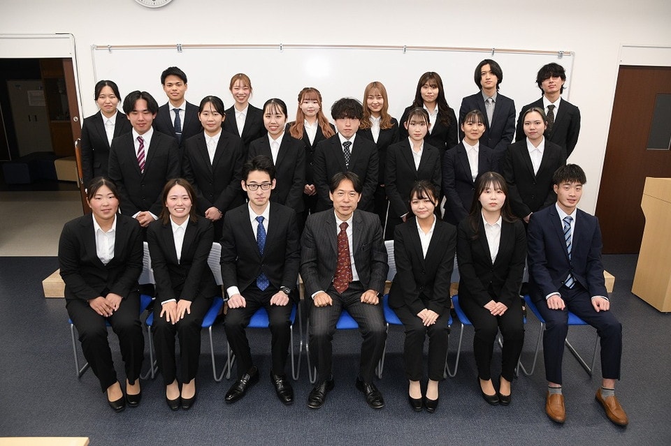 写真：スーツ姿で集合写真を撮る学生たちと教員