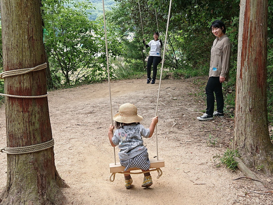 ブランコに乗る子どもを見守る学生