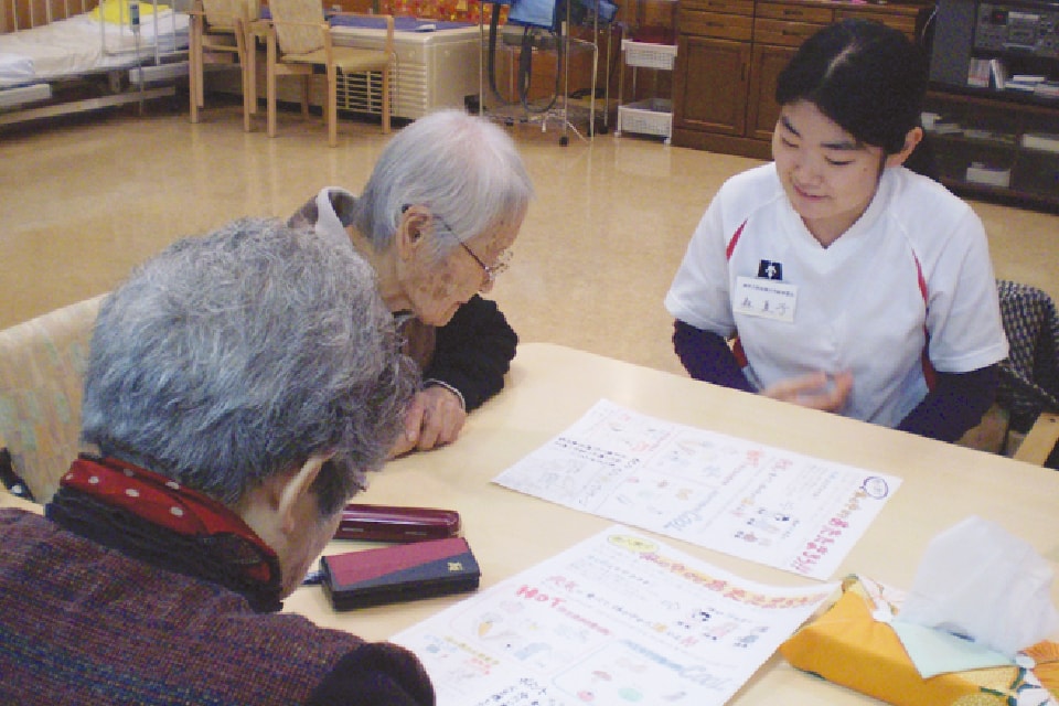 写真：女性が老人2人と机の上の資料を見ながら話を聞いている様子