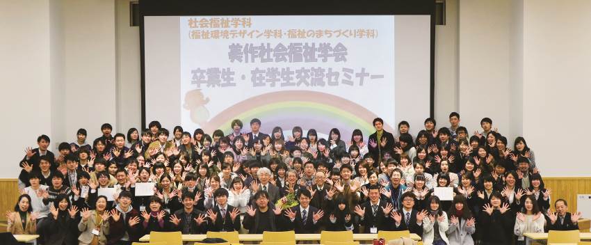 写真：「美作社会福祉学科 卒業生・在学生交流セミナー」と映し出されたスクリーンの前に集合する学生たち