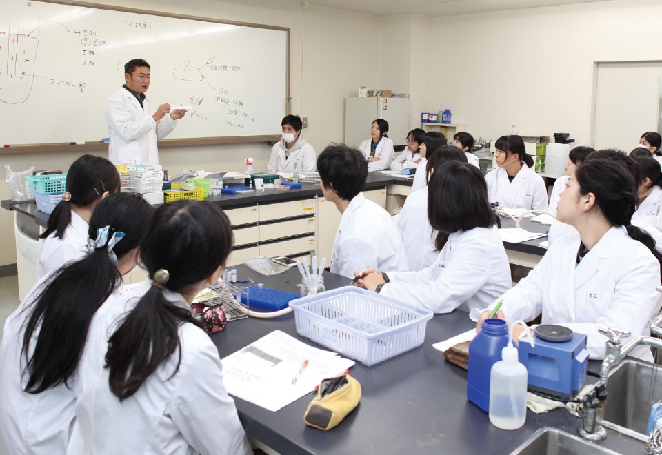 写真：男性教員と生徒たちが実習(講義)を受けている様子。