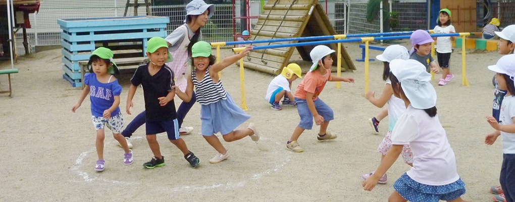 写真：園庭で元気よく遊ぶ園児たちと先生