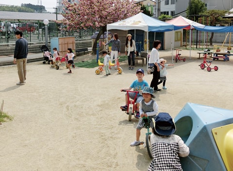 写真：遊具を使うなどして園庭で思い思いに遊ぶ園児たちと保護者